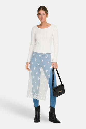 Jupe blanche ONLY, avec détails en dentelle, portée sur un jean bleu à broderies florales et des bottes noires.