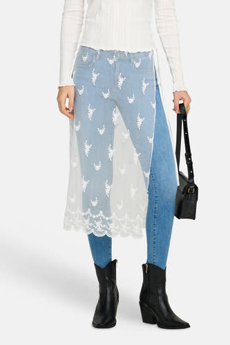 Witte rok van ONLY, met kanten details, gedragen over een blauwe jeans met bloemenborduursel en zwarte laarzen.