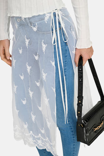 Jupe blanche ONLY avec broderie florale sur un jean bleu, associée à un sac à main noir.