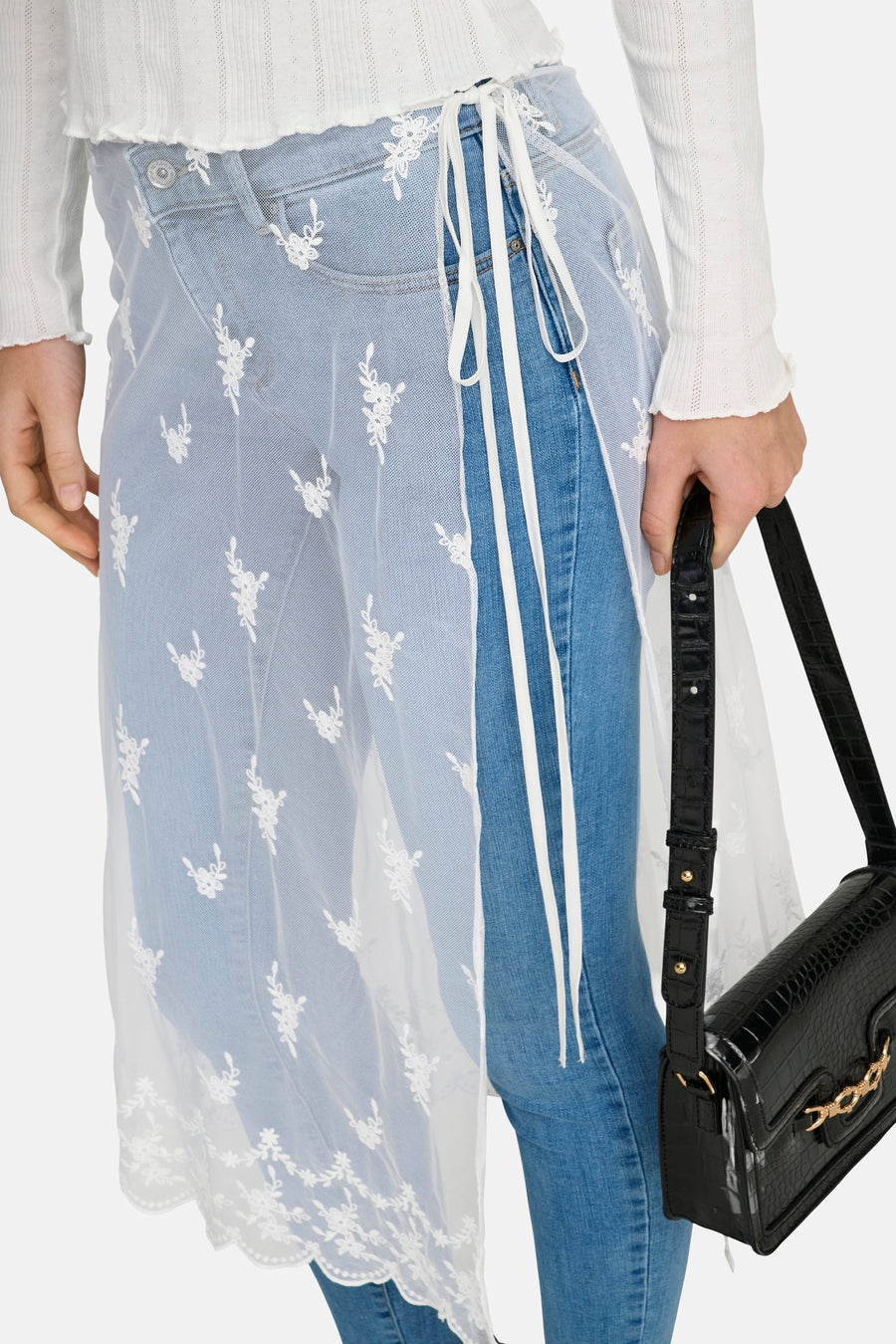 Jupe blanche ONLY avec broderie florale sur un jean bleu, associée à un sac à main noir.