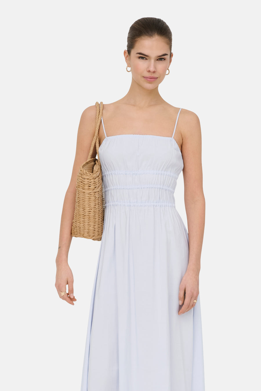 Robe bleue sans manches ONLY® avec bretelles spaghetti et détails smockés, portée avec un sac en osier.