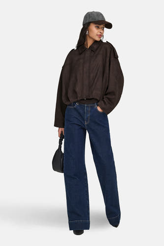 Manteau brun de JDY, avec une coupe décontractée et un col, associé à un pantalon en cuir et un chapeau.