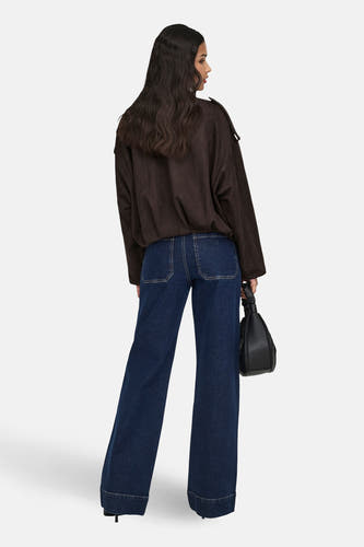 Manteau court brun de JDY, avec des manches longues, un col et porté avec un jeans foncé et un chapeau.