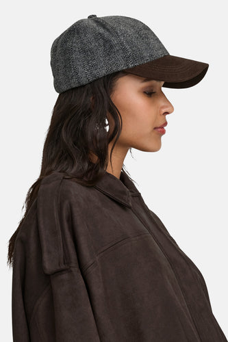 Vrouw met pet en bruine jas van suède, in profiel.