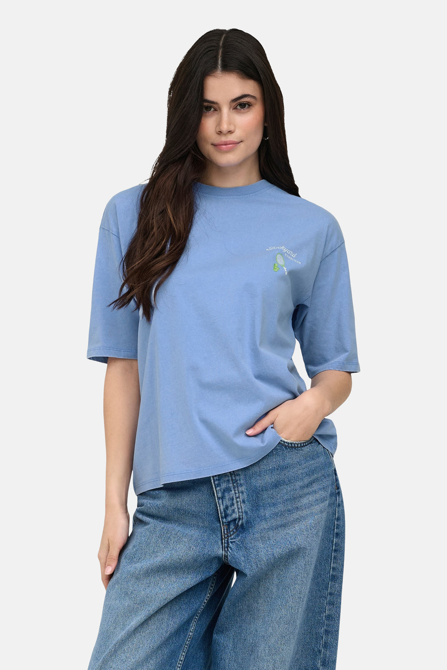 T-shirt bleu ONLY® avec imprimé 'Backyard tennis tour', porté par un mannequin avec un jean ample et des baskets blanches.
