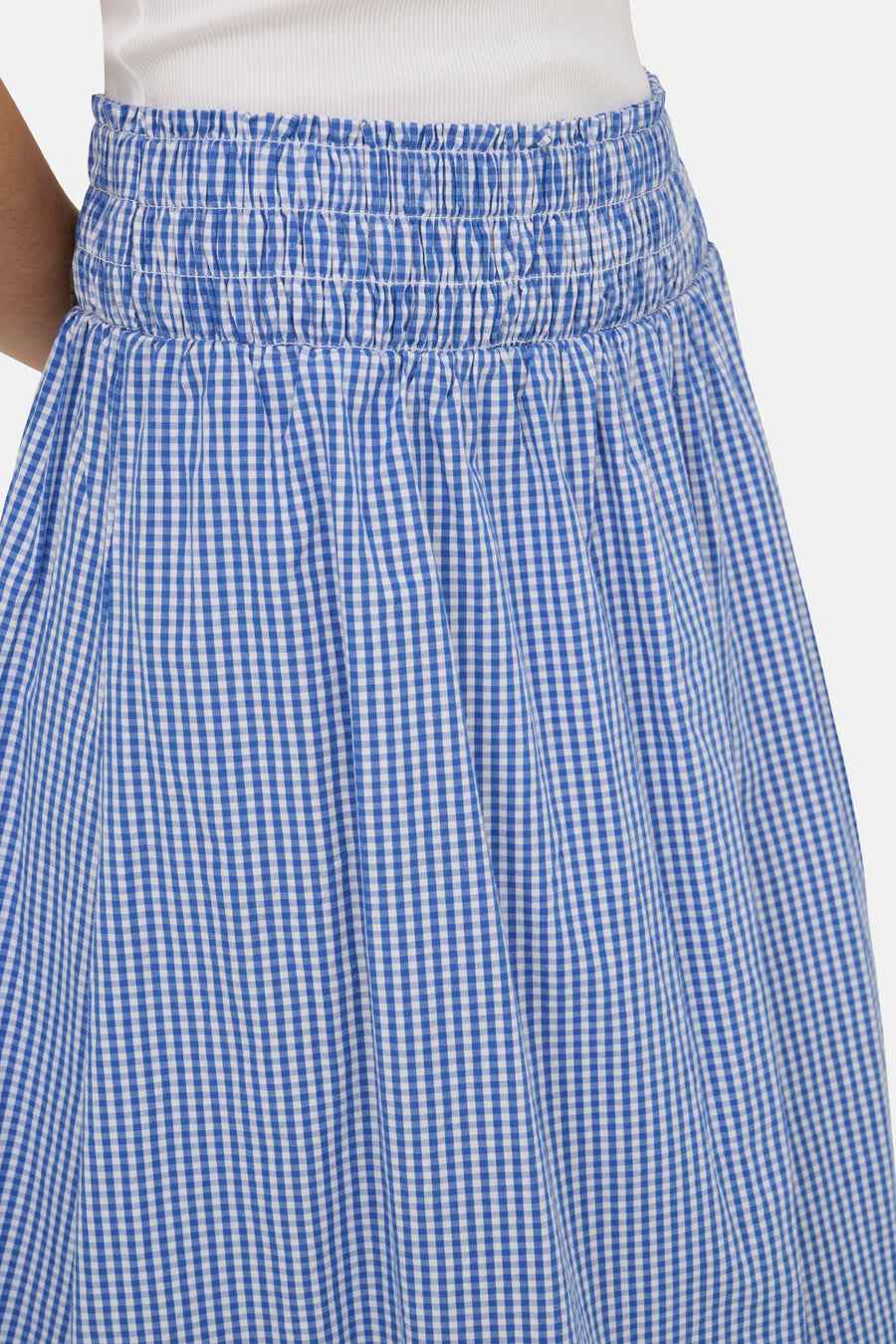 Jupe bleue à motif à carreaux vichy de ONLY, avec taille smockée, portée avec un haut blanc.