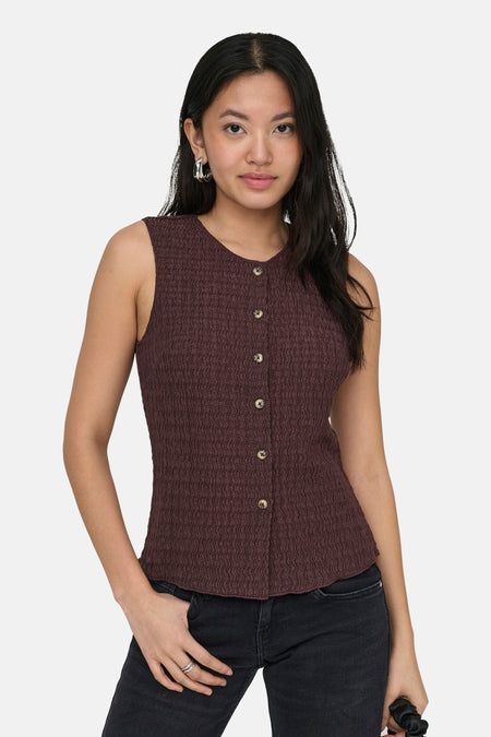 Gilet marron de ONLY®, avec fermeture à boutons et texture structurée, combiné avec un jean noir et des boucles d'oreilles argentées.