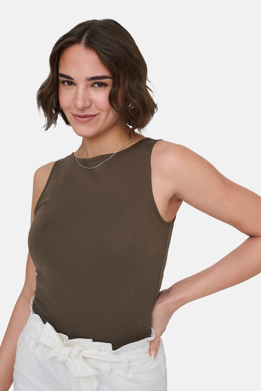Haut marron sans manches de ONLY, avec un col rond et porté avec une chaîne argentée et un pantalon blanc.