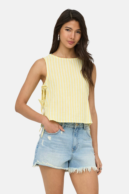 Chemisier sans manches à rayures jaunes de ONLY® avec détails de nœud, porté avec un short en jean et des tongs jaunes.