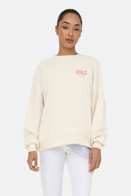 Pull beige à col rond de ONLY® avec motif de poisson brodé et 'Sardines', coupe oversize, porté sur un haut en dentelle bleu clair.