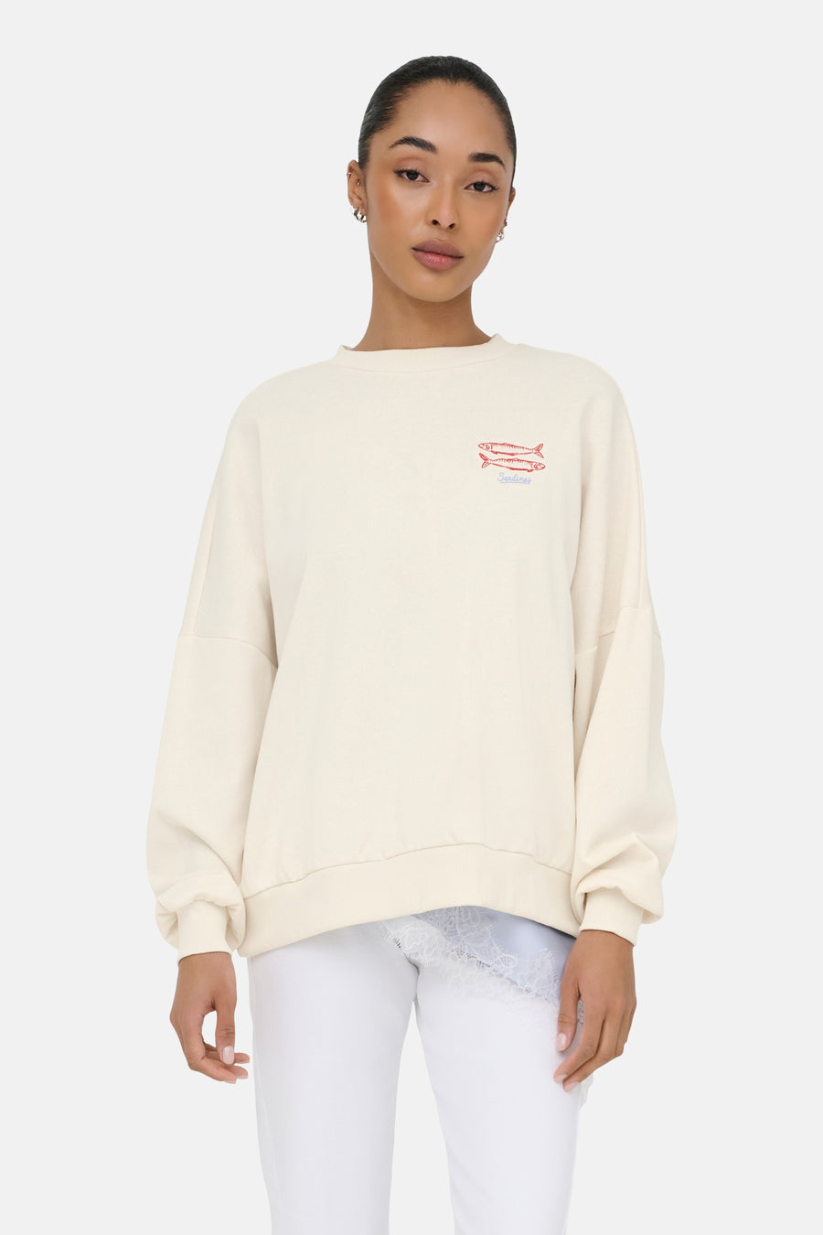 Pull beige à col rond de ONLY® avec motif de poisson brodé et 'Sardines', coupe oversize, porté sur un haut en dentelle bleu clair.