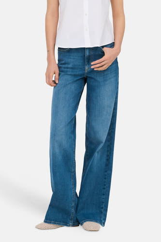 Jean large MADISON BLUSH bleu moyen en denim de ONLY, avec une main dans la poche, et une chemise blanche.