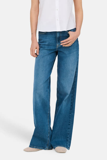 Jean large MADISON BLUSH bleu moyen en denim de ONLY, avec une main dans la poche, et une chemise blanche.