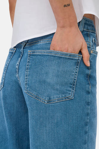 Jean large bleu d'ONLY, avec une main dans la poche arrière, porté avec une chemise blanche.