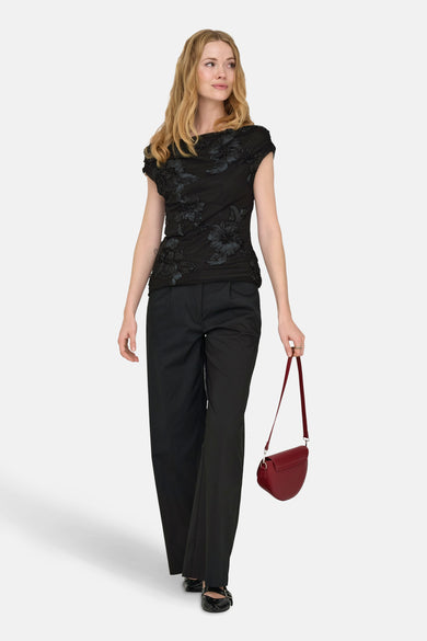 Blouse noire à manches courtes de JDY, avec un motif floral et portée avec une jupe noire et une poche rouge.