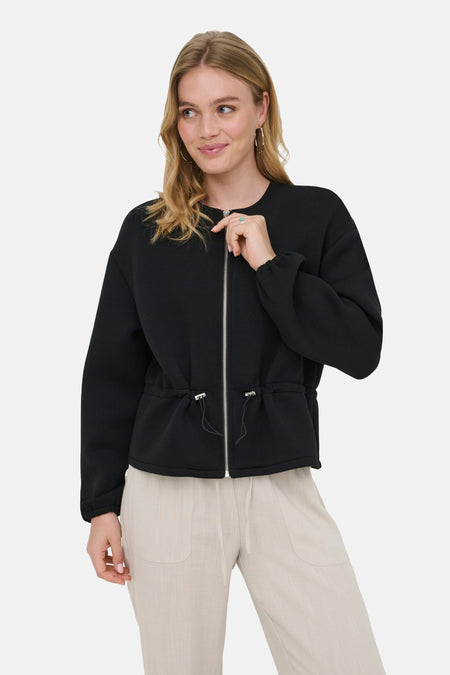 Veste courte noire ONLY® avec fermeture éclair sur le devant et cordon de serrage à la taille, portée avec un pantalon beige.