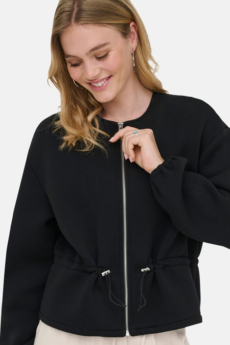 Veste courte noire ONLY® à col rond, fermeture éclair intégrale et cordon de serrage à la taille, portée par une femme souriante.