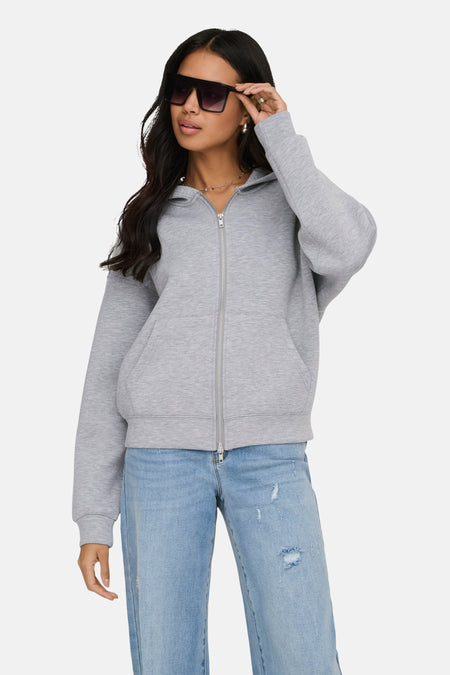 Gilet-pull gris ONLY®, avec fermeture éclair et manches longues, combiné avec un jean et des lunettes de soleil.