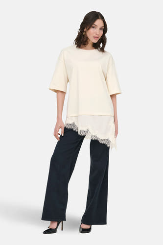 T-shirt beige à manches courtes de JDY, avec détails de bords asymétriques et combiné avec un pantalon noir et des talons.