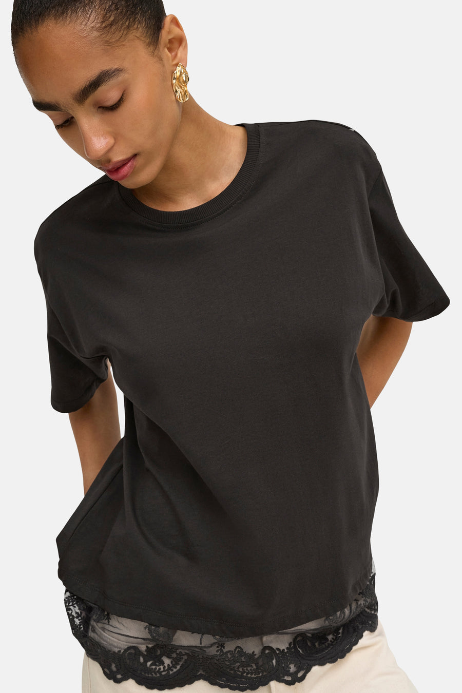 Zwart korte mouwen T-shirt van ONLY® met ronde hals, gladde stof en lichte pasvorm, gedragen met gouden oorbellen en kanten detail aan onderkant.