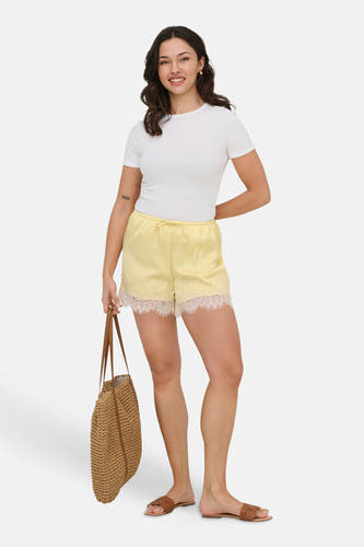 Gele satijnlook korte broek van ONLY® met elastische taille, trekkoord en witte kanten rand, gedragen met wit T-shirt.