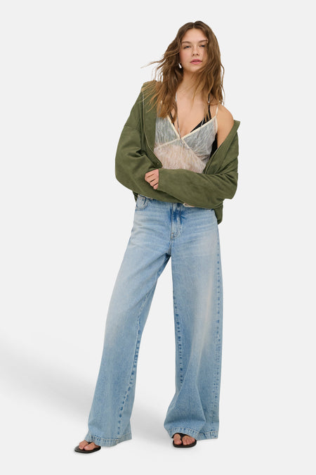 Chemisier en dentelle écru de ONLY® avec bretelles spaghetti, porté sous une veste verte ouverte et un jean ample.