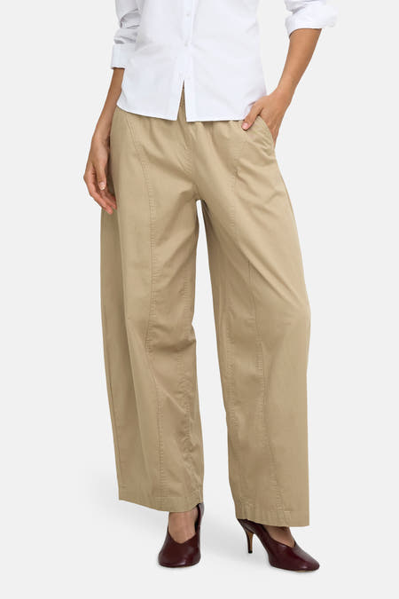 Beige wijde broek van JDY, voorzien van zijnaad details, gedragen met wit overhemd en bordeauxhoge hakken, front view.