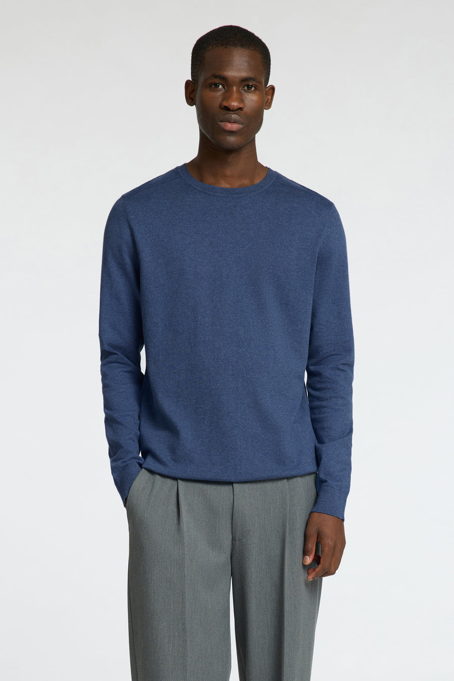 Pull bleu à col rond de SELECTED, combiné avec un pantalon gris, debout sur un fond blanc.