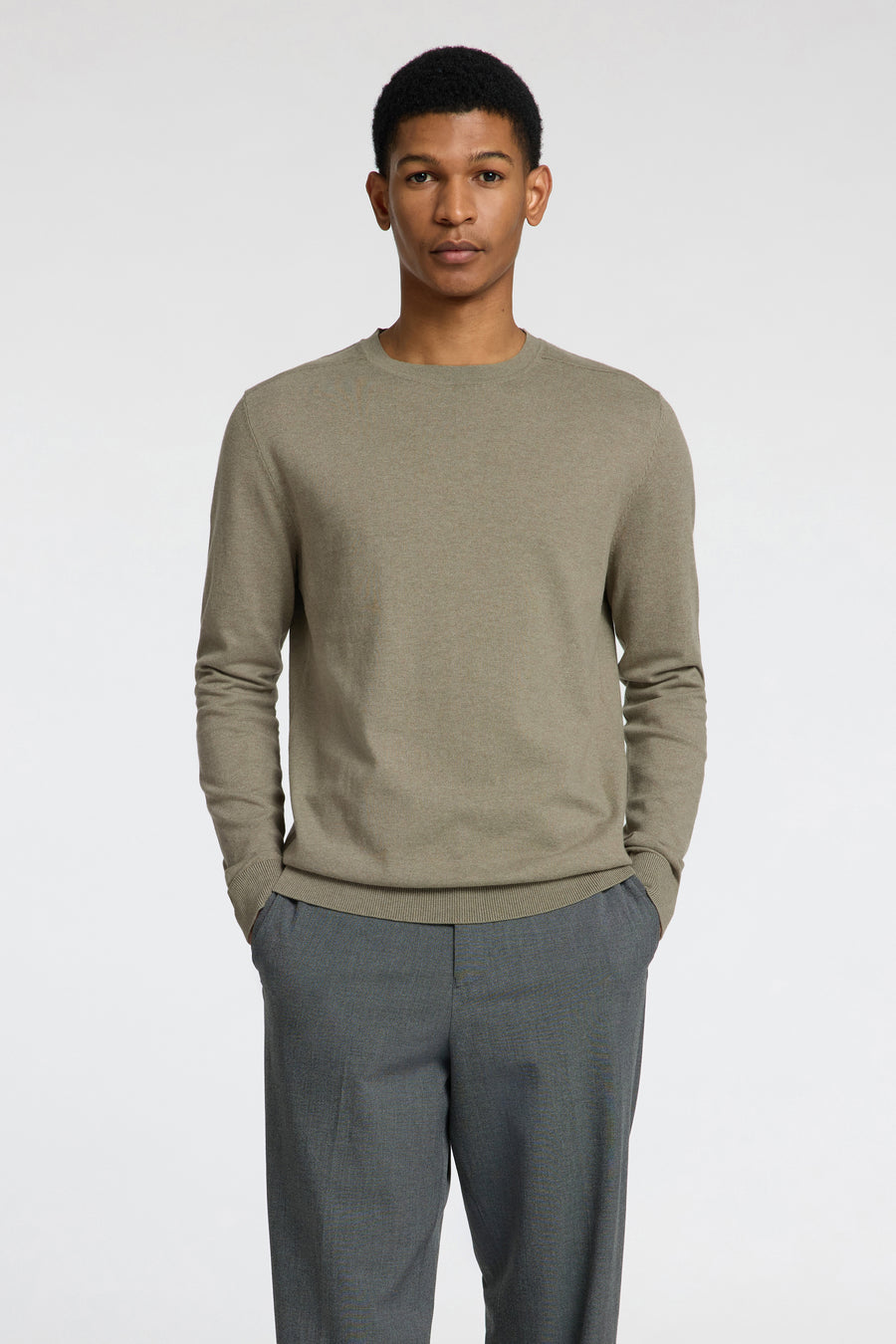 Pull vert avec col rond de SELECTED, combiné avec un pantalon gris, représenté debout sur un fond blanc.