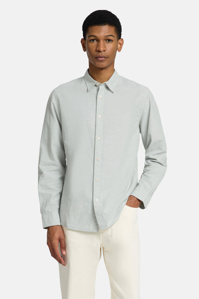 Chemise verte à manches longues de SELECTED, avec col boutonné et portée avec des pantalons blancs et des chaussures marron.