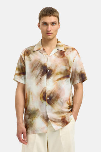 Chemise brune à manches courtes de SELECTED, avec un motif abstrait, portée avec des shorts beige et des sandales.