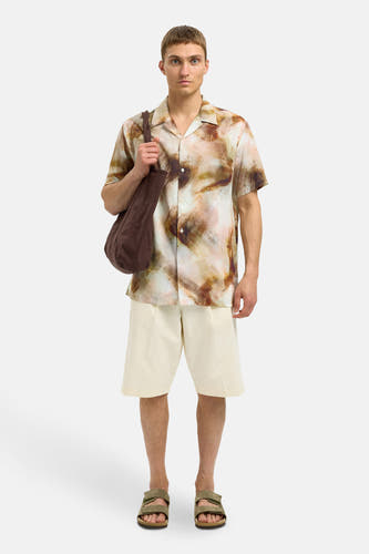 Chemise brune à manches courtes de SELECTED, avec un motif abstrait en aquarelle, portée avec des shorts écru et des sandales kaki.