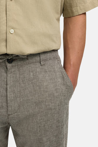Pantalon marron de SELECTED avec une texture finement tissée et une main dans la poche.