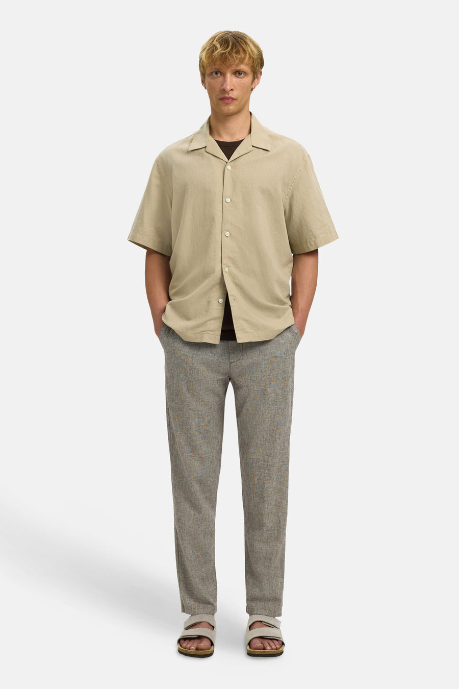 Pantalon marron de SELECTED, avec un motif chiné subtil, combiné avec une chemise beige et des sandales.