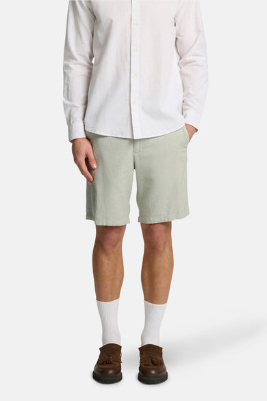 Short vert de SELECTED, combiné avec un chemisier rayé, des chaussettes blanches et des loafers marrons.
