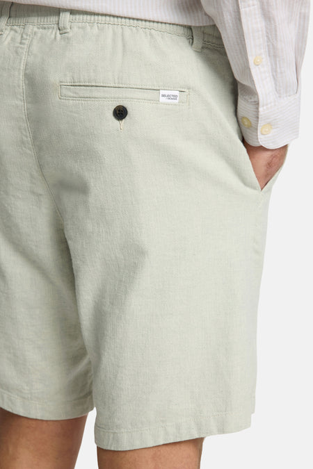 Short vert de SELECTED / HOMME, avec un détail de bouton et une poche poante, en gros plan.