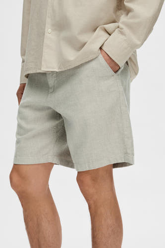 Short vert de SELECTED, avec une texture légère, des poches latérales et porté avec une chemise beige.
