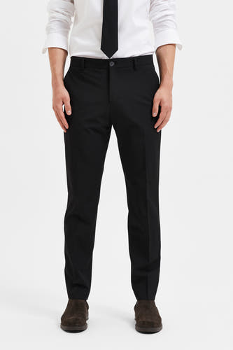 Pantalon de costume noir de SELECTED, avec une coupe classique et des détails subtils, combiné avec une chemise blanche et une cravate.