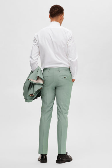 Groene kostuumbroek van SELECTED, met een blazer over de arm en zwarte schoenen.
