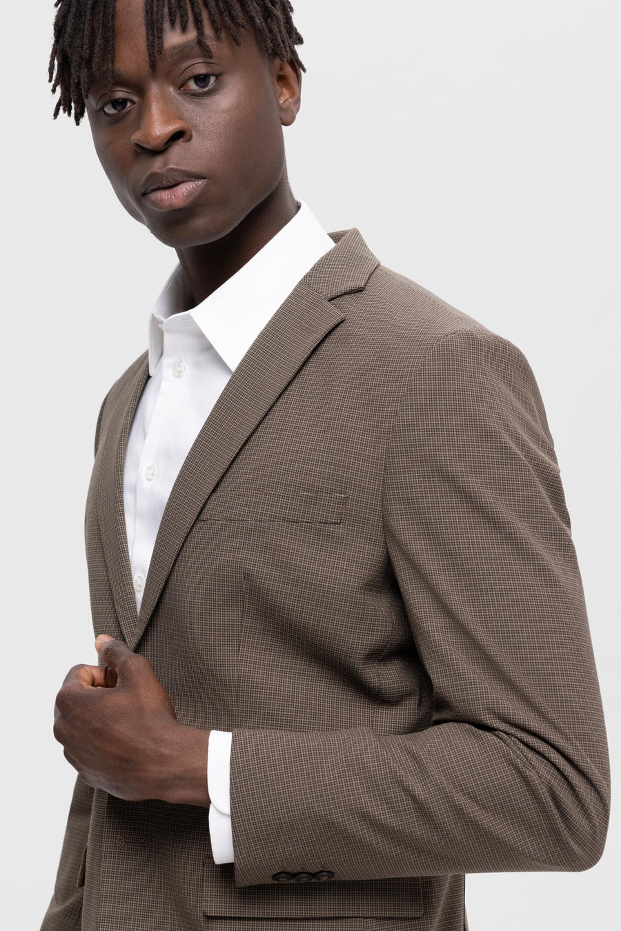 Man in bruin geruit jas met wit overhemd.

