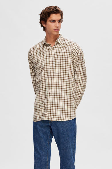 Chemise brune à longues manches de SELECTED, avec un motif à carreaux, portée avec des jeans bleus et des chaussures en cuir de suède.