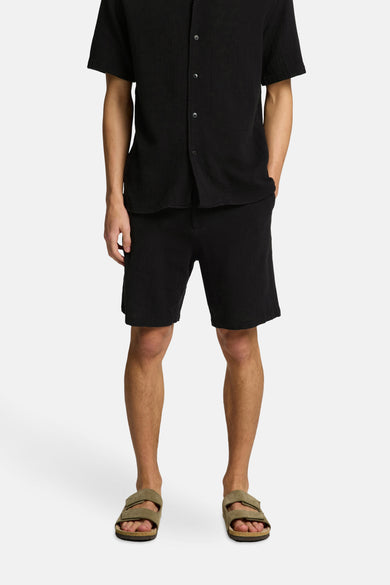 Short noir de SELECTED, porté avec un chemisier noir et des sandales brunes.