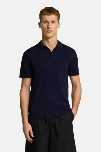 Polo bleu à manches courtes de SELECTED, porté avec des shorts noirs et des sandales marrons.