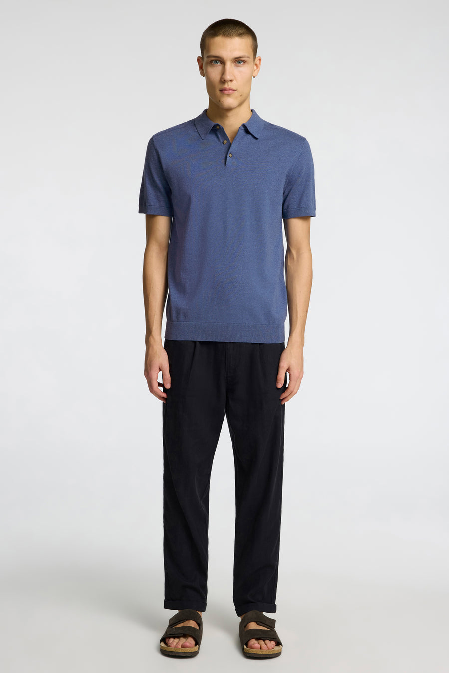 Polo bleu à manches courtes de SELECTED, tricotée, portée avec un pantalon noir et des sandales marron foncé.