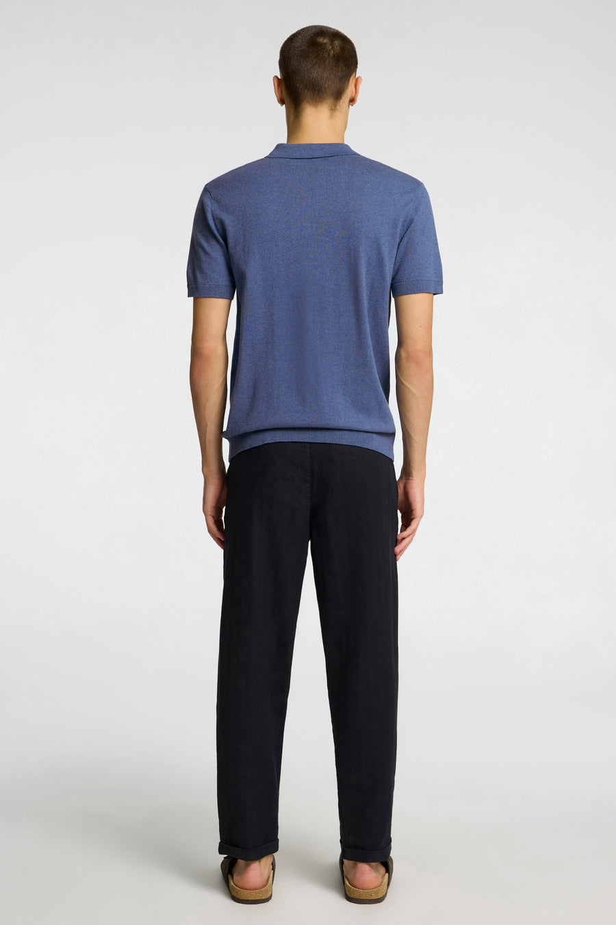 Polo bleu à manches courtes de SELECTED, porté par un homme, vue de dos, avec un pantalon noir et des sandales marron.