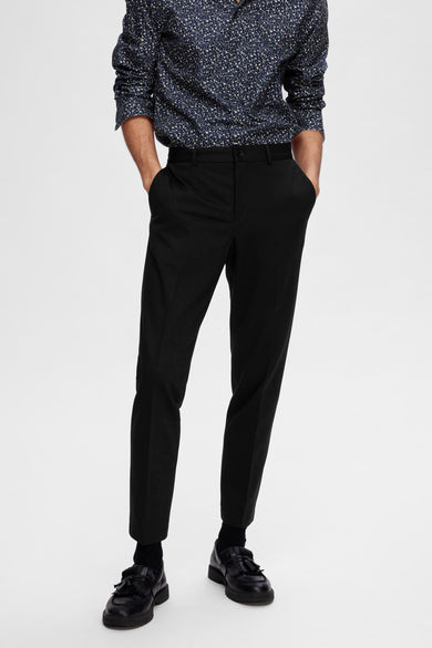 Pantalon de costume noir SELECTED, porté avec un chemisier bleu à fleurs et des loafers noirs.