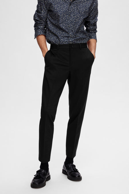 Pantalon de costume noir SELECTED, porté avec un chemisier bleu à fleurs et des loafers noirs.