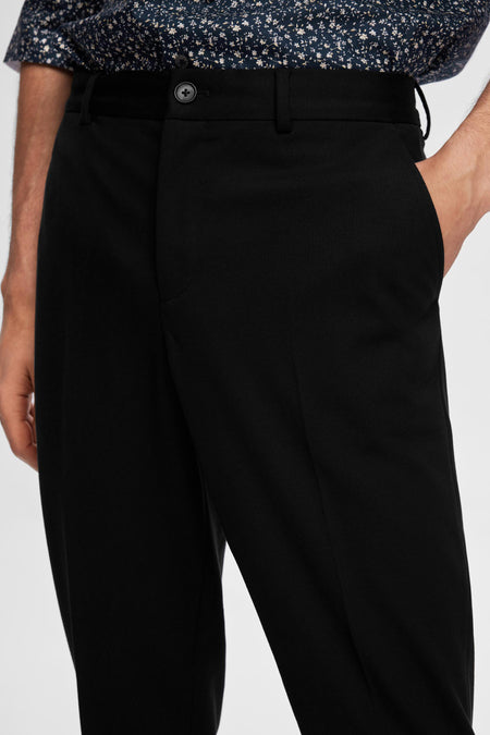 Pantalon de costume noir SELECTED, porté avec les mains dans les poches, associé à une chemise à motifs floraux.