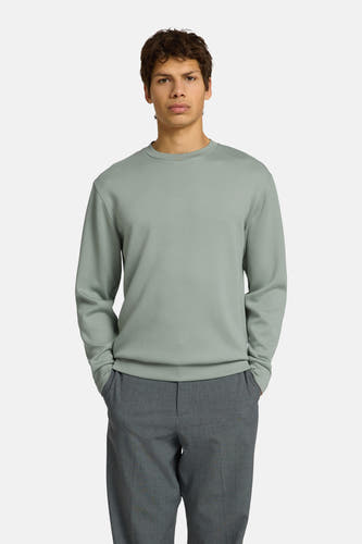 Pull vert avec col rond de SELECTED, en tissu lisse, porté par un homme avec un pantalon gris foncé et des mocassins noirs.
