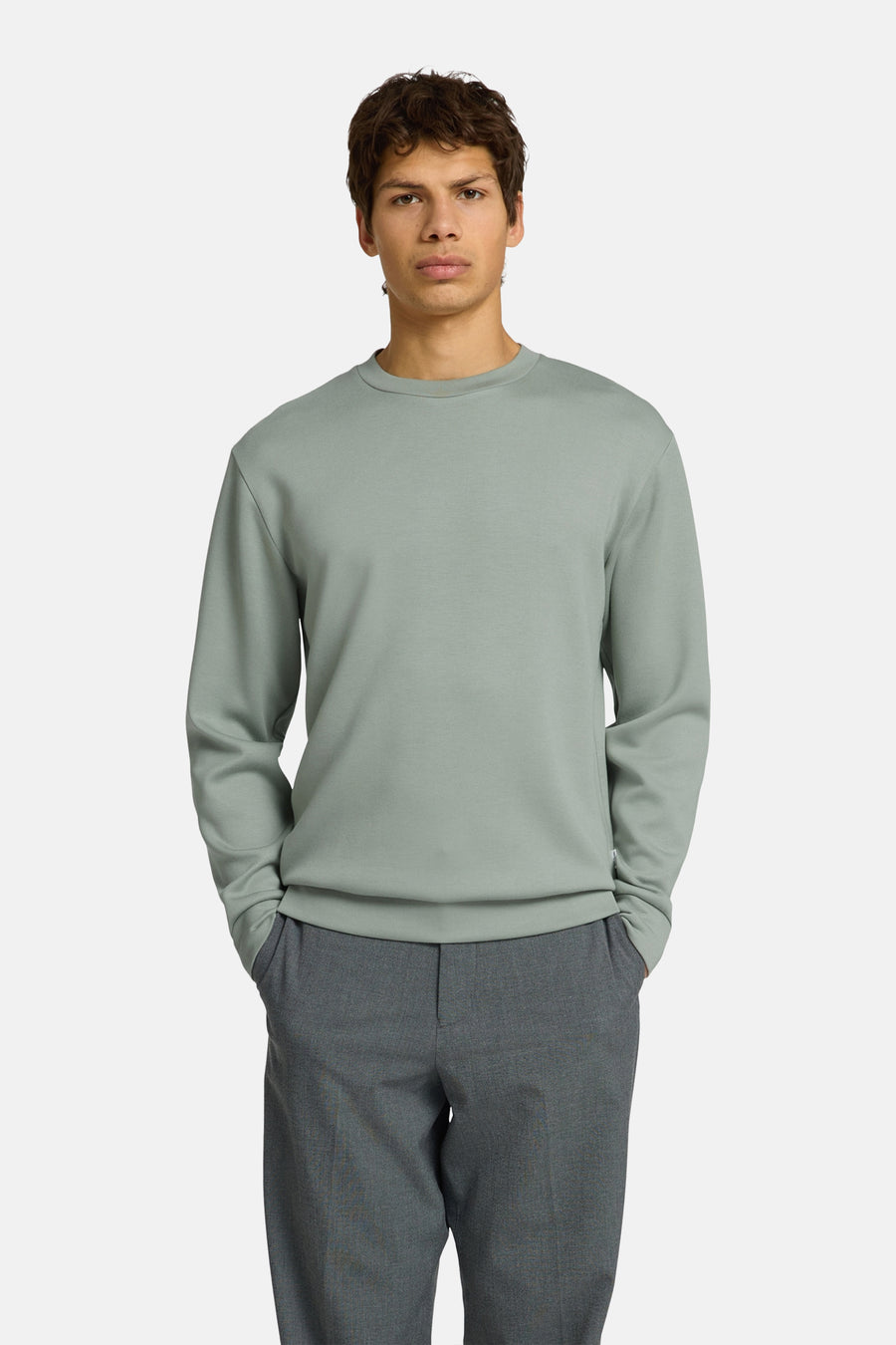 Pull vert avec col rond de SELECTED, en tissu lisse, porté par un homme avec un pantalon gris foncé et des mocassins noirs.